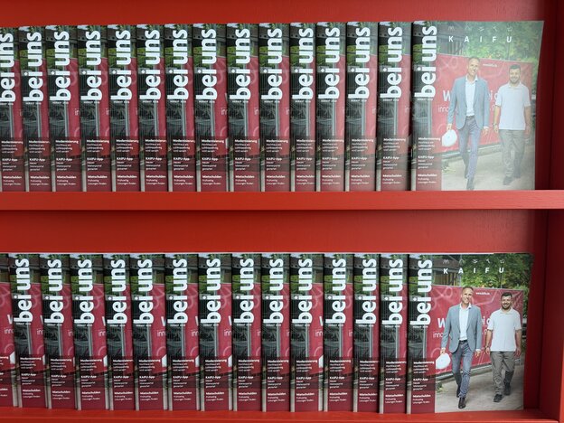 Mehrere Ausgaben des KAIFU-Mitgliedermagazins „bei uns“ stehen nebeneinander aufgereiht in einem roten Regal.