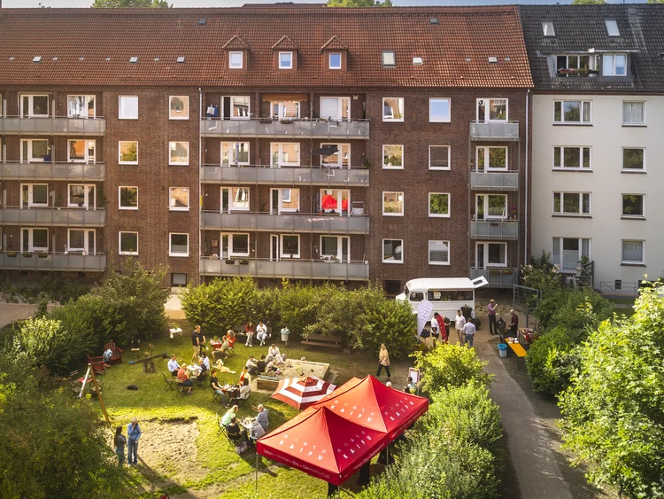 Vogelperspektive auf ein Sommerfest im grünen Innenhof einer Wohnanlage mit rotem Zelt, Tischen und feiernden Menschen.