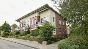 Schrägansicht des Wohnhauses von der Straße aus gesehen, umgeben von gepflegten Grünanlagen und Bäumen.