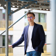 Eric Yeung-Schüürmann, kaufmännischer Vorstand der KAIFU, lächelt auf einem Baugerüst vor einem modernen Wohngebäude.