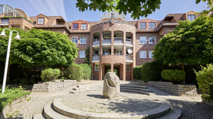 Gepflasterter Innenhof mit Steinskulptur vor halbrunder Klinkerfassade